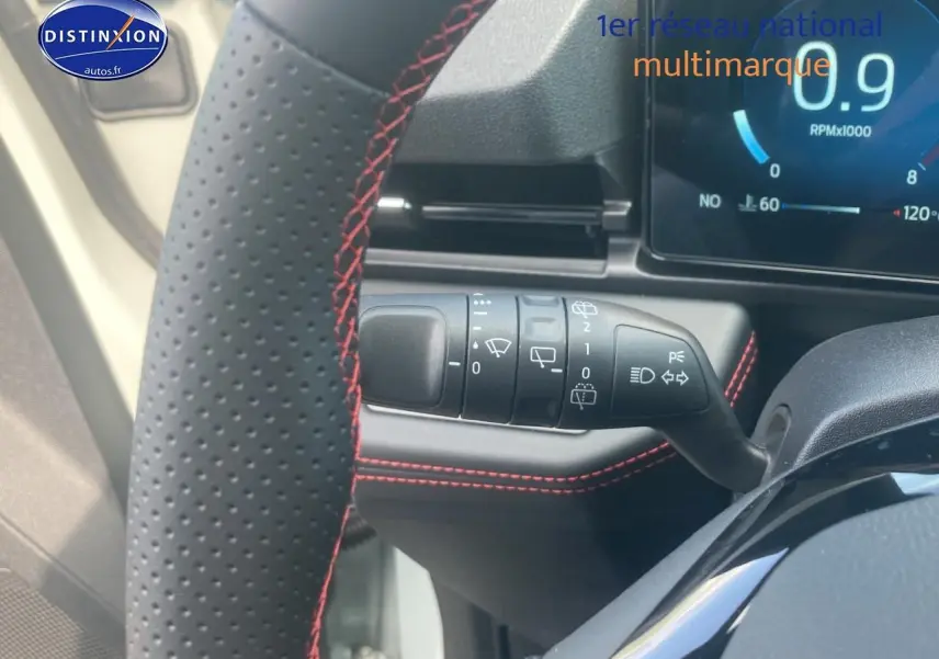 Gros plan sur le volant perforé noir avec surpiqûres rouges et la commande des essuie-glaces du Ford Puma gris cactus 2025.