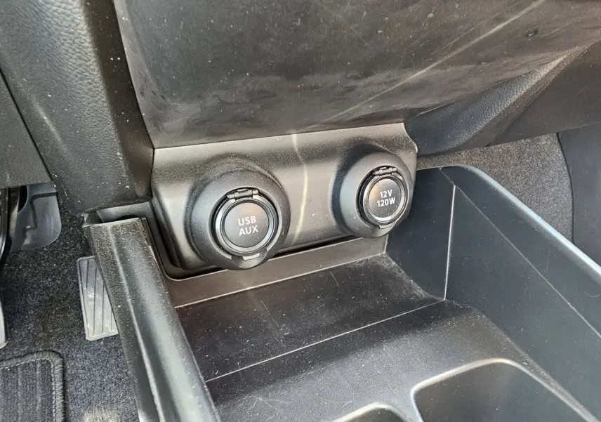 Vue rapprochée de la console centrale avant de la Suzuki Swift 2023 montrant les prises USB/AUX et 12V sous le tableau de bord.