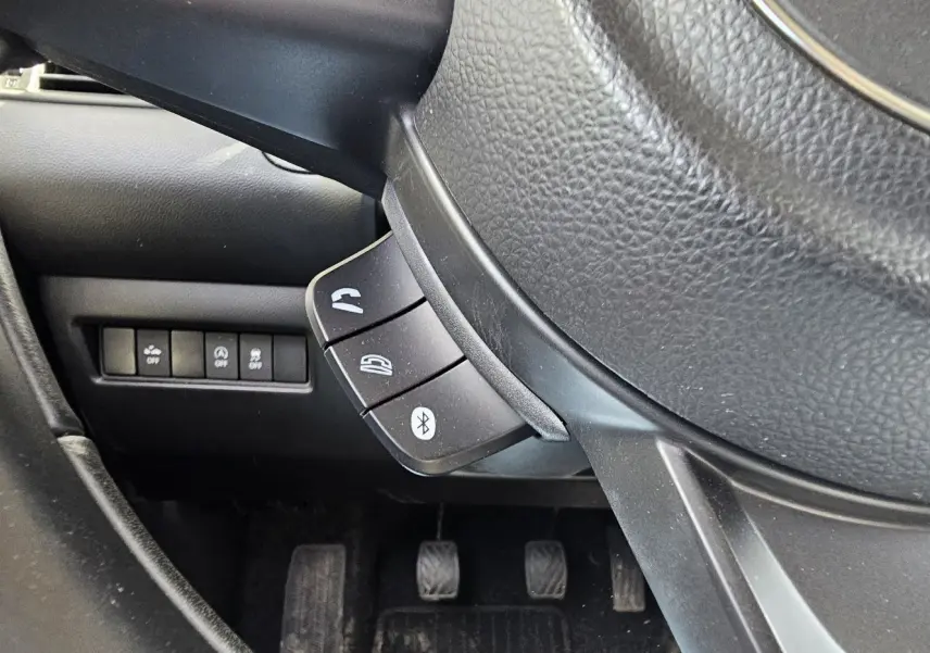 Gros plan sur le volant noir de la Suzuki Swift 2023, montrant les commandes Bluetooth et téléphone côté gauche.