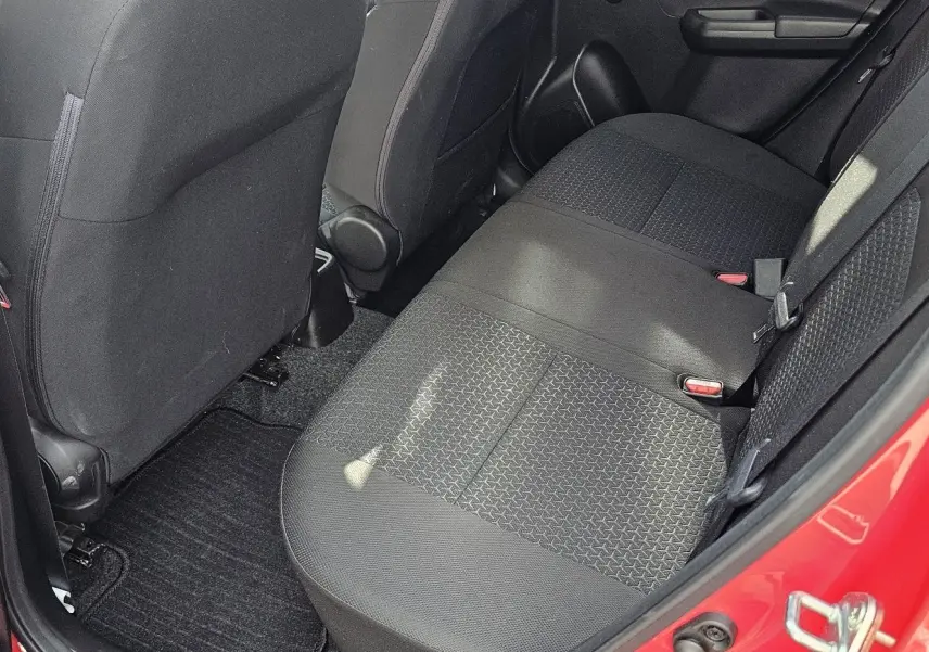 Vue intérieure côté arrière droit montrant la banquette arrière noire et la portière rouge vif d'une Suzuki Swift 2023.