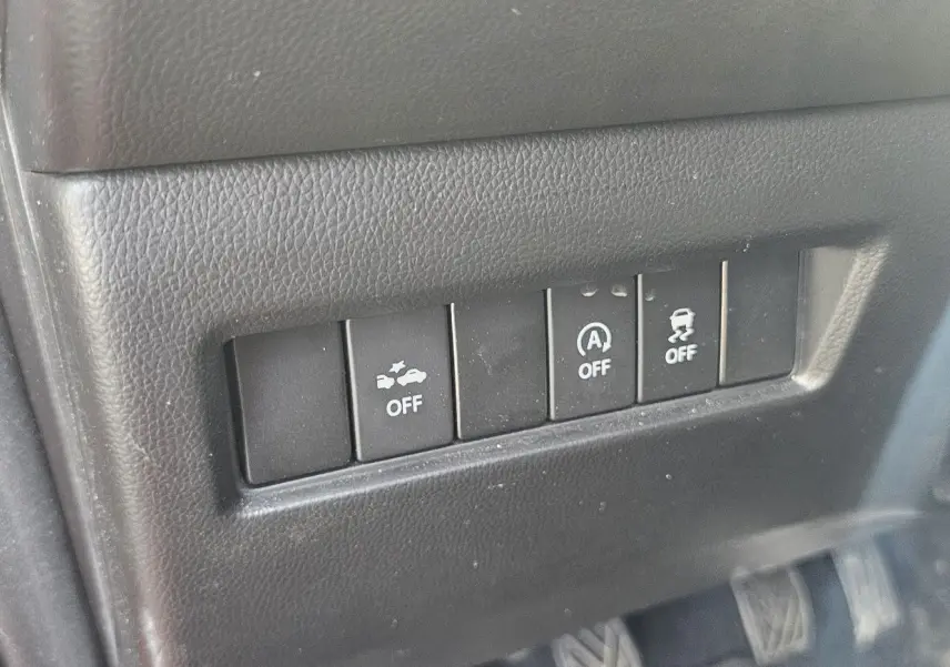 Gros plan sur les boutons de contrôle d'assistance à la conduite dans une Suzuki Swift rouge, intérieur noir texturé.