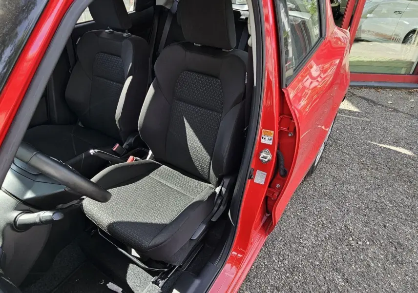 Vue intérieure côté conducteur de la Suzuki Swift 2023 rouge fervent, mettant en valeur les sièges noirs en tissu.