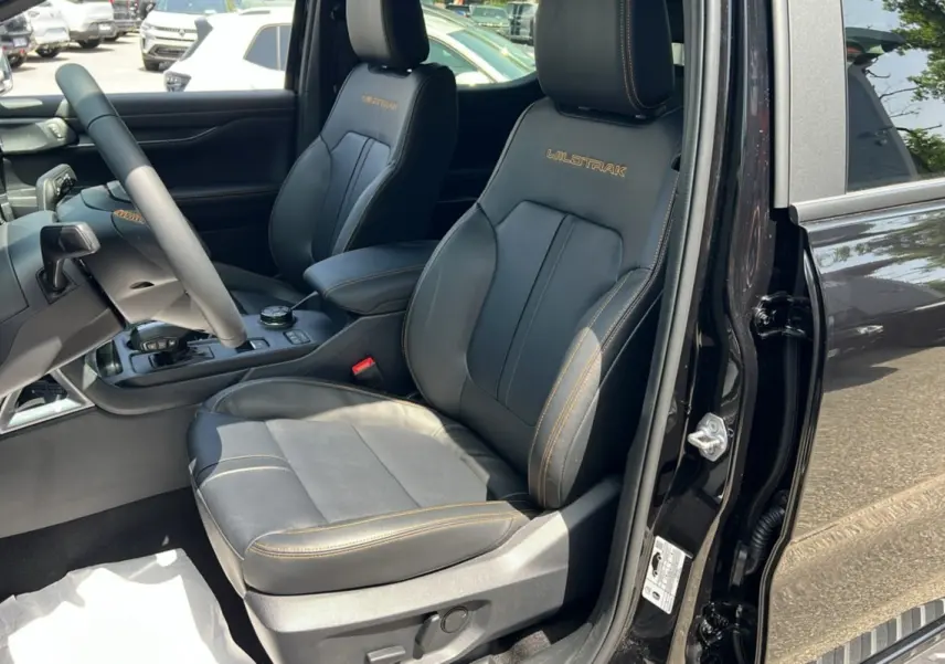 Intérieur côté conducteur du Ford Ranger 2025 Wildtrak Plus noir agate, sièges en cuir avec surpiqûres orange et logo Wildtrak.