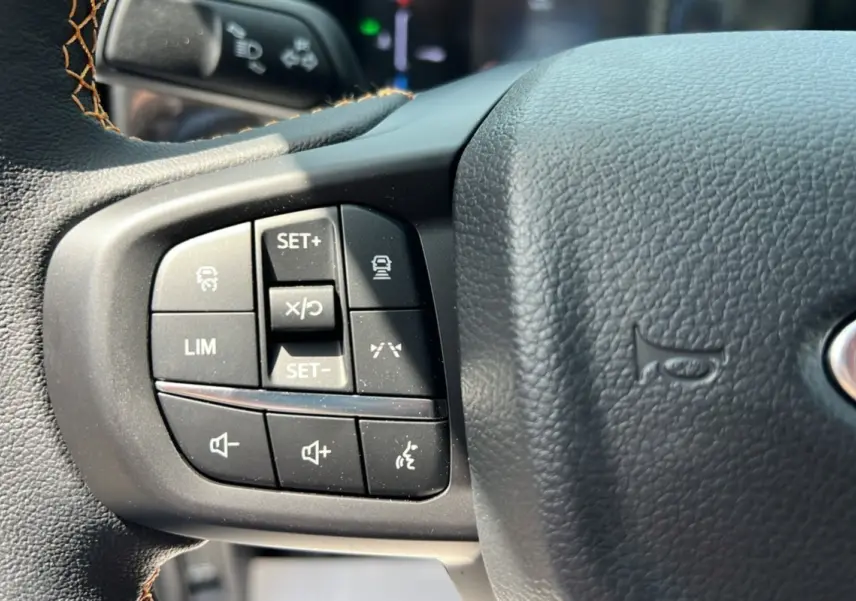 Gros plan sur les commandes au volant du Ford Ranger 2.3 PHEV 281 Wildtrak Plus 2025, cuir noir avec surpiqûres marron.
