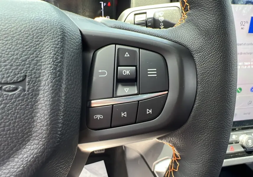 Gros plan sur les commandes au volant du Ford Ranger 2.3 PHEV Wildtrak Plus 2025 en cuir noir avec surpiqûres orange.