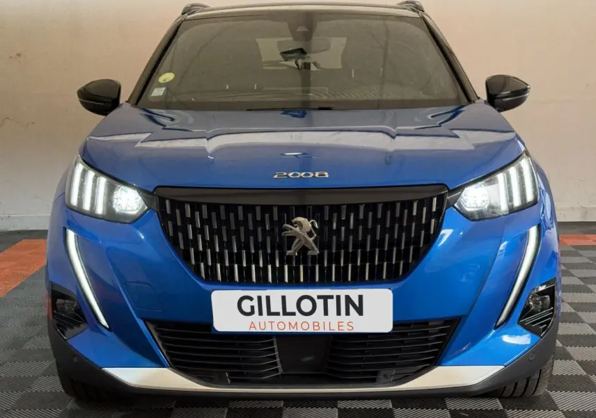 Vue avant d'un Peugeot 2008 bleu avec phares LED allumés et calandre noire distinctive, en intérieur.