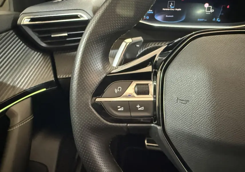 Gros plan sur le volant cuir perforé et les commandes multifonctions à gauche du Peugeot 2008 GT Pack bleu, avec tableau de bord numérique.