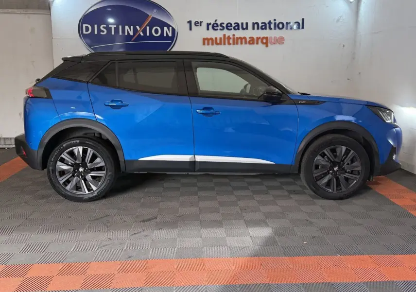 Peugeot 2008 bleu en profil droit, toit noir et jantes alliage, dans un showroom intérieur.