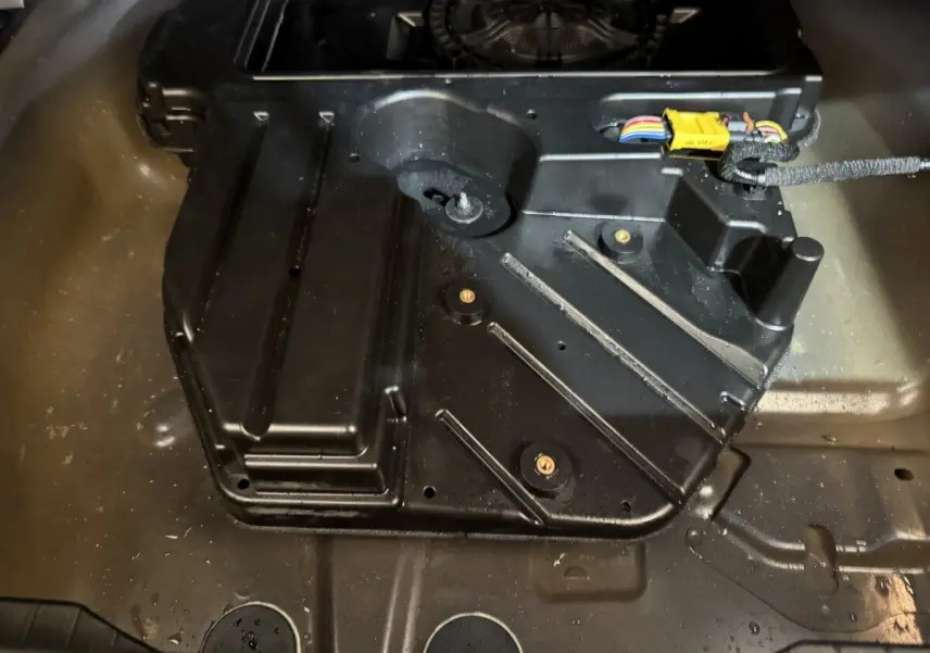 Vue rapprochée du compartiment de rangement sous le plancher du coffre du Peugeot 2008 bleu, avec câblage visible.