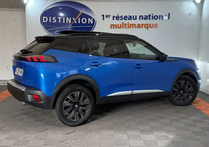 Vue côté droit arrière d'un Peugeot 2008 bleu 2021 avec toit noir et jantes noires dans un showroom.