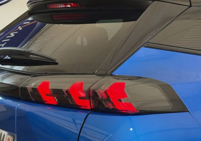 Feu arrière droit allumé sur Peugeot 2008 bleu, vue rapprochée du coin arrière avec lunette et essuie-glace.