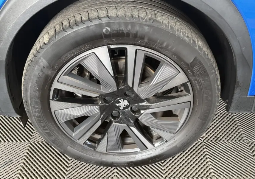 Gros plan sur la roue avant droite d’un Peugeot 2008 bleu, mettant en valeur la jante alliage au design moderne.