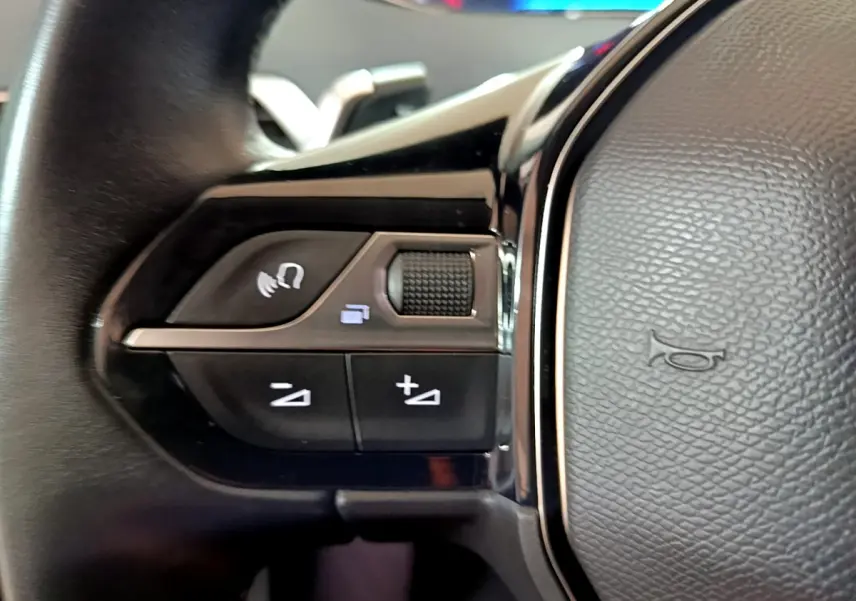 Gros plan sur les commandes gauche du volant cuir du Peugeot 5008 gris clair, avec boutons de volume et téléphone.