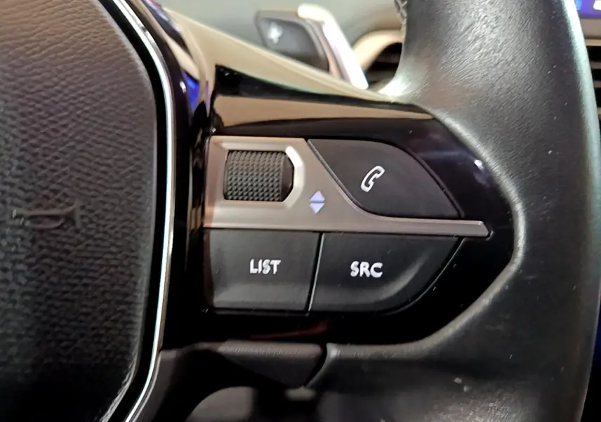 Gros plan sur les commandes gauche du volant cuir noir du Peugeot 5008 gris clair, boutons appel et liste audio visibles.