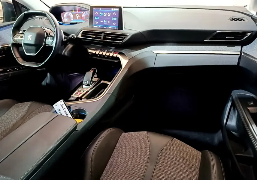 Intérieur Peugeot 5008 gris clair vu côté passager, tableau de bord moderne avec écran tactile et volant compact cuir.