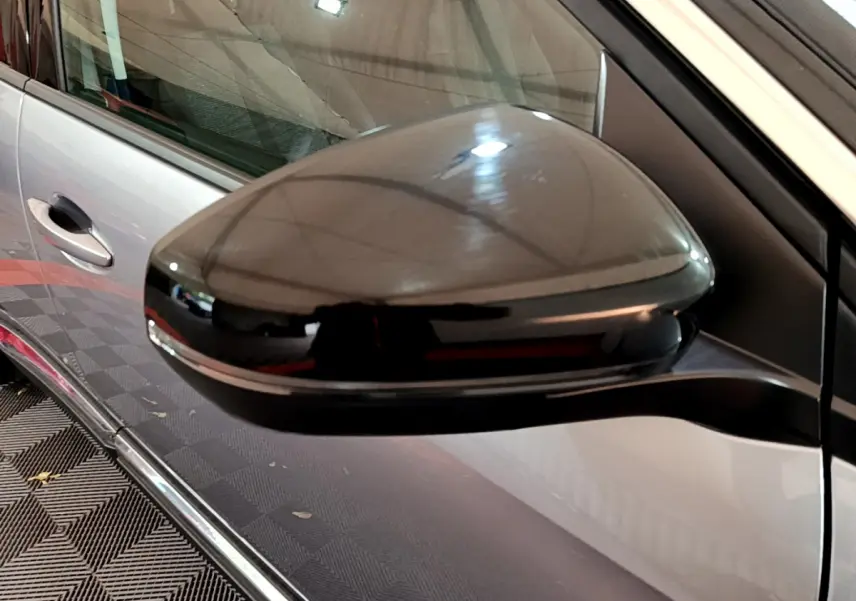 Rétroviseur noir brillant côté conducteur d’un Peugeot 5008 gris clair vu de près en intérieur.