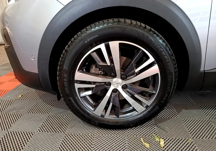 Gros plan sur la roue arrière droite du Peugeot 5008 gris clair, avec jante alliage bicolore et logo Peugeot central.