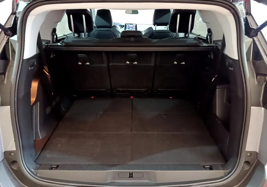 Coffre spacieux ouvert vu de l'arrière d'un Peugeot 5008 gris clair, avec sièges arrière relevés et tablette de coffre.