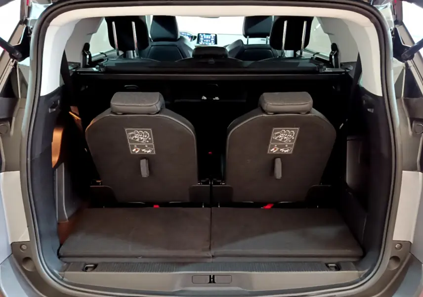 Vue arrière du coffre ouvert d'un Peugeot 5008 gris clair, montrant la 3ème rangée de sièges individuels relevés.