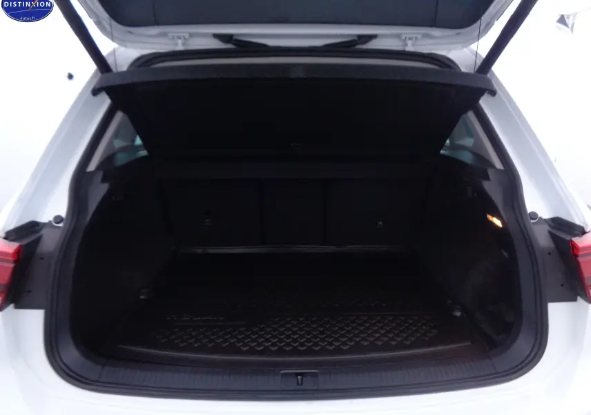 Coffre ouvert vu de l'arrière d'un Volkswagen Tiguan blanc 2019, espace de chargement noir avec tapis de protection.