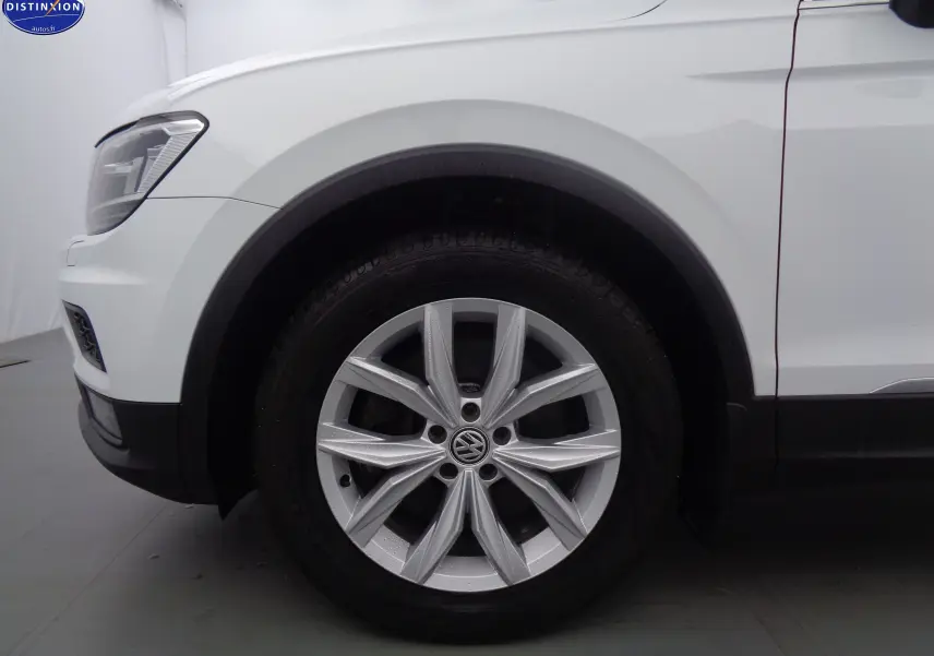 Gros plan sur la roue avant gauche d'un Volkswagen Tiguan blanc 2019, mettant en valeur la jante alliage et le passage de roue.