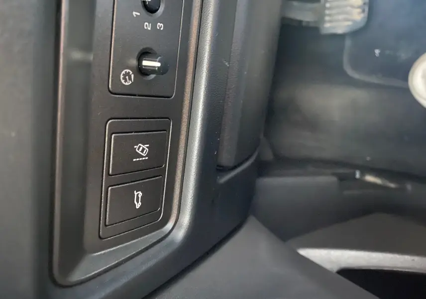 Gros plan sur les commandes de réglage et ouverture du coffre côté conducteur dans l'habitacle noir d'un Range Rover Evoque blanc.