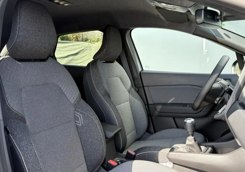 Intérieur du Renault Captur 2025 vu côté droit, sièges tissu gris avec volant et levier de vitesses manuelle visibles.