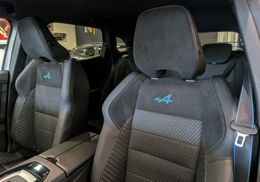 Gros plan sur les sièges avant en cuir noir et alcantara avec logo Alpine bleu du Renault Austral 2025 full hybride.