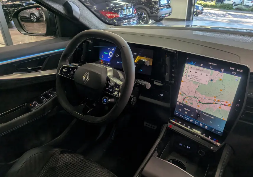 Vue intérieure côté conducteur du Renault Austral hybride 2025, avec tableau de bord numérique et grand écran tactile central affichant une carte.
