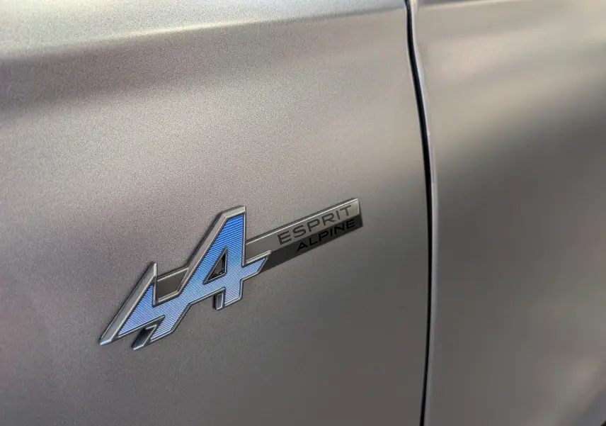 Gros plan sur l'emblème Esprit Alpine bleu sur la porte gris schiste satin du Renault Austral 2025 hybride.