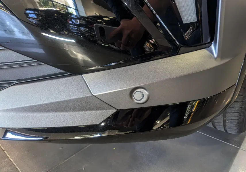 Détail du pare-chocs avant gris schiste satin et noir du Renault Austral hybride, avec capteur de stationnement visible.