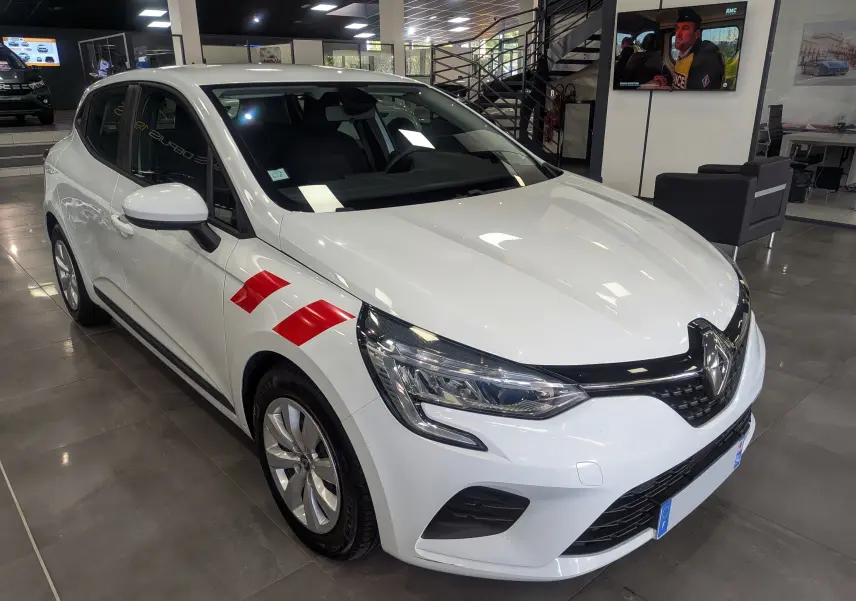 Renault Clio V blanche vue en 3/4 avant droit avec bandes rouges sur l'aile, exposée en showroom.