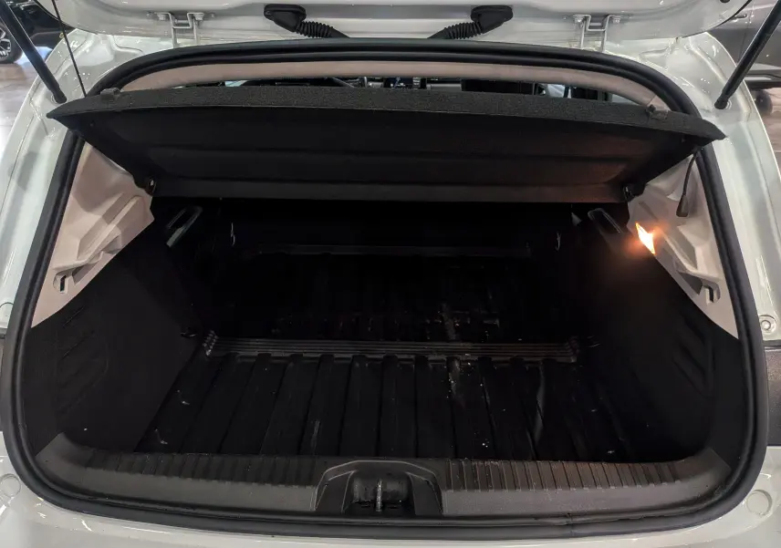 Coffre ouvert vu de l'arrière d'une Renault Clio V blanche, montrant un espace de chargement noir et éclairé à droite.