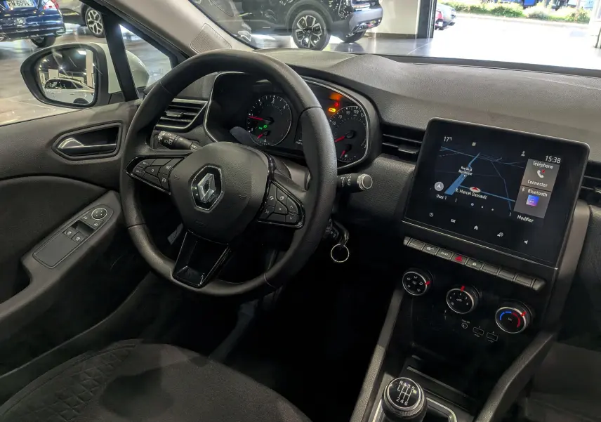 Vue intérieure côté conducteur de la Renault Clio V blanche avec tableau de bord, volant multifonction et écran tactile GPS.