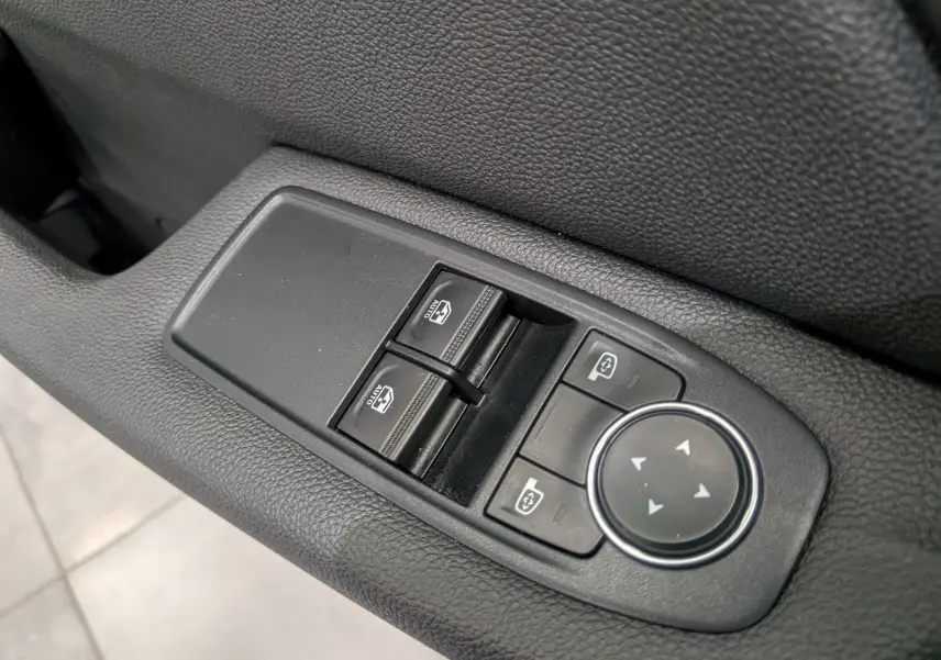 Gros plan sur les commandes des vitres électriques et réglages des rétroviseurs côté conducteur d'une Renault Clio V blanche.