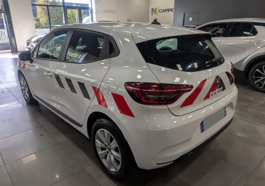 Vue 3/4 arrière droite d'une Renault Clio V blanche avec bandes rouges et noires distinctives sur la carrosserie.