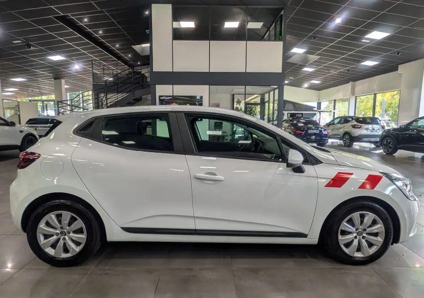 Profil côté gauche d'une Renault Clio V blanche Glacier avec bandes rouges sur l'aile avant, en intérieur showroom.
