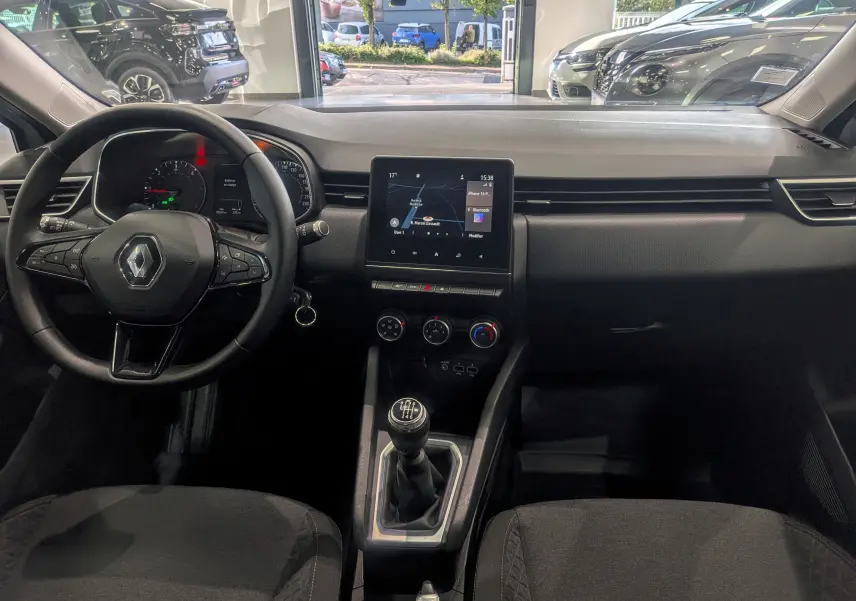 Intérieur de la Renault Clio V blanche, vue frontale du tableau de bord avec écran tactile et levier de vitesse manuel.