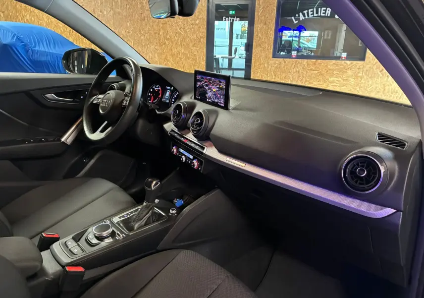 Vue intérieure côté conducteur de l'Audi Q2 35 TFSI S-Line 2023 noire, avec tableau de bord et écran GPS central.