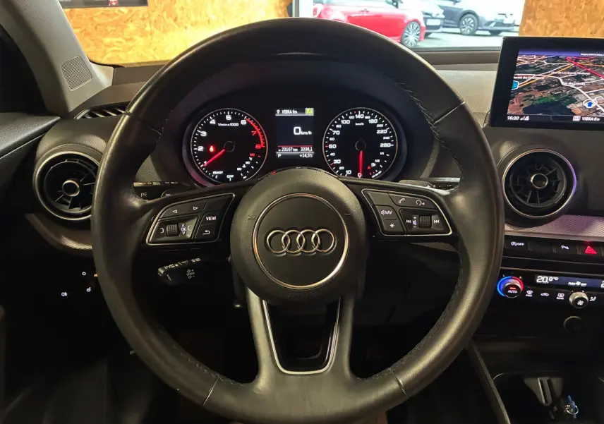Vue intérieure centrée sur le volant cuir Audi d'un Q2 35 TFSI noir, avec tableau de bord digital et écran GPS à droite.