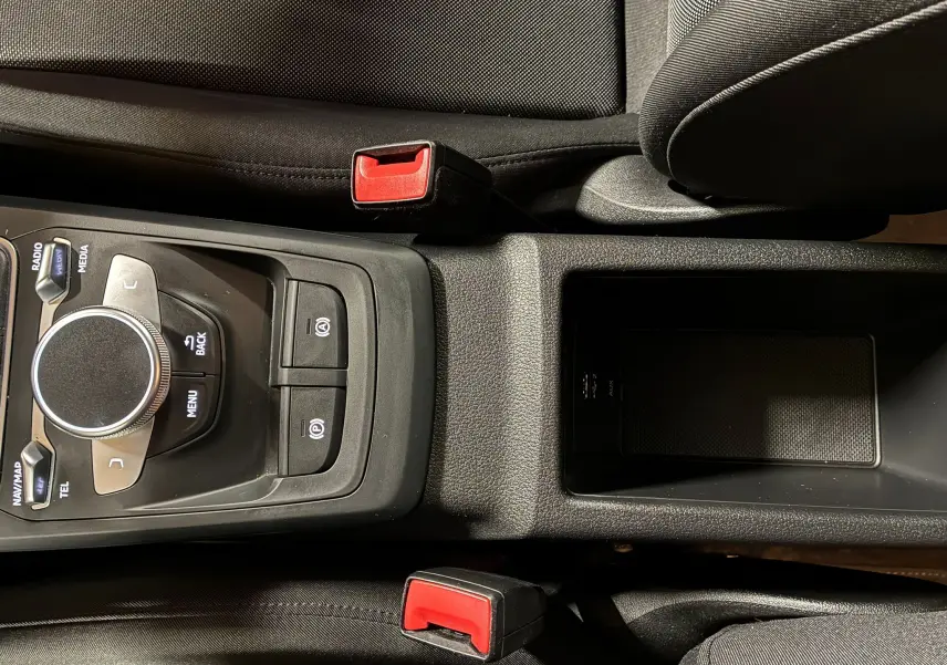 Vue rapprochée de la console centrale noire de l'Audi Q2 35 TFSI S-Line 2023 avec commandes multimédia et ceintures rouges.