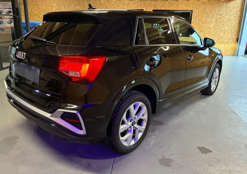 Audi Q2 noir vue 3/4 arrière droit dans un garage, avec feux arrière allumés et jantes argentées.