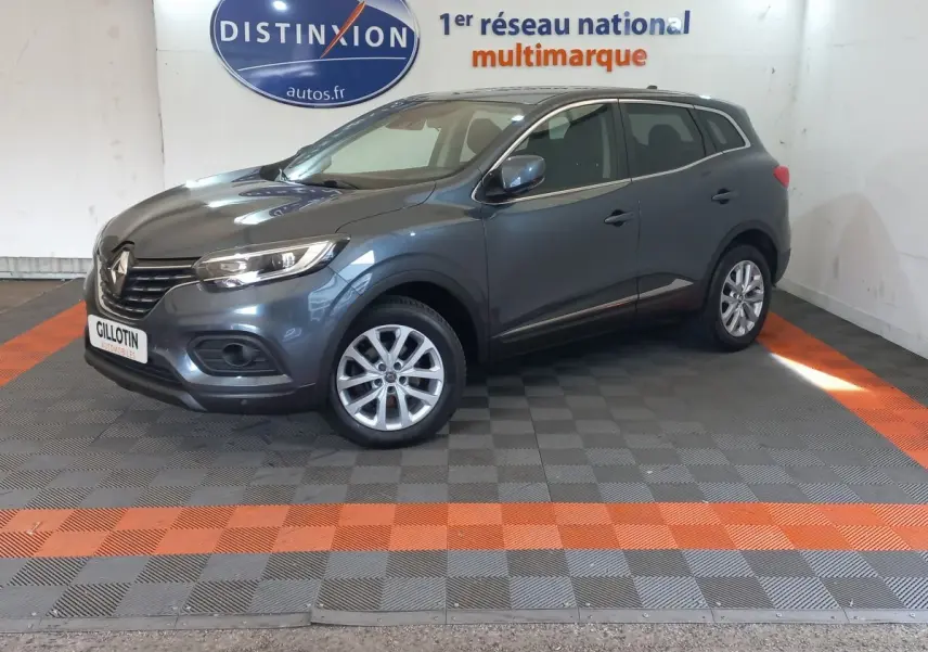 Renault Kadjar Business gris foncé en 3/4 avant droit, avec jantes alliage et phares LED visibles en intérieur showroom.