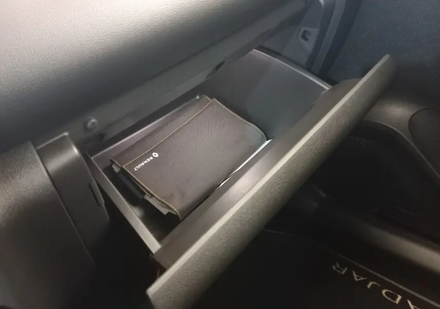 Gant de boîte à gants ouvert côté passager dans un Renault Kadjar gris foncé, avec pochette Renault visible.