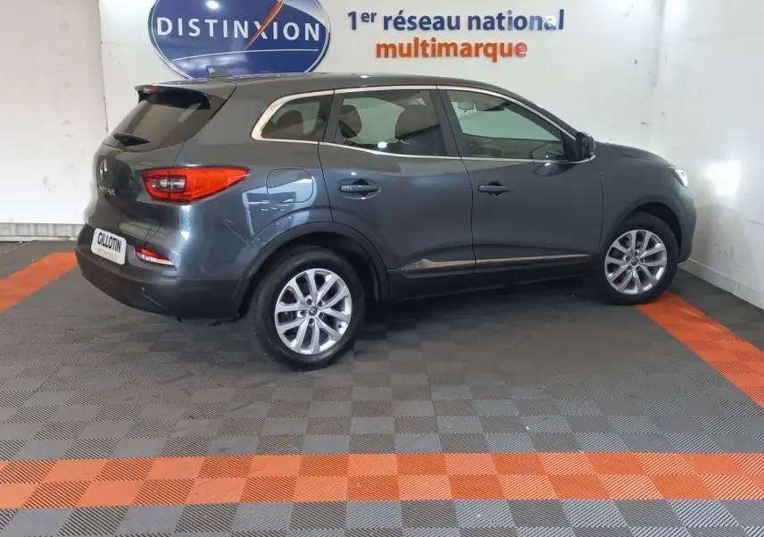 Vue côté droit d'un Renault Kadjar Business gris foncé 2022, avec jantes alliage et feux arrière visibles en intérieur showroom.