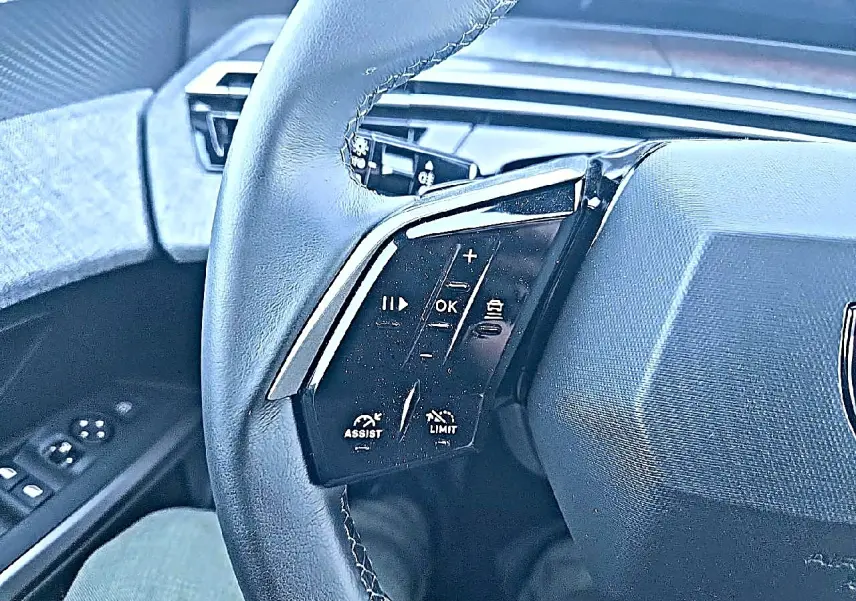 Gros plan sur le volant cuir noir du Peugeot 5008 Hybrid 145 allure, avec commandes multifonctions visibles côté gauche.