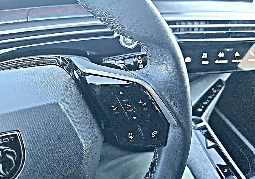 Gros plan sur le volant cuir multifonction noir du Peugeot 5008 Hybrid 145 allure e-dcs6 avec commandes vocales et téléphone.