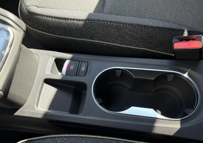 Gros plan sur la console centrale noire du Renault Captur blanc nacré 2025 avec porte-gobelets et commandes de frein à main électrique.