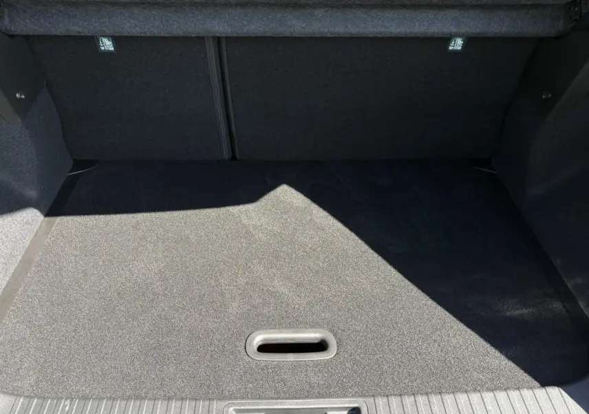 Coffre spacieux du Renault Captur blanc nacré 2025 vu de l'intérieur, avec plancher de coffre mobile et tapis gris.