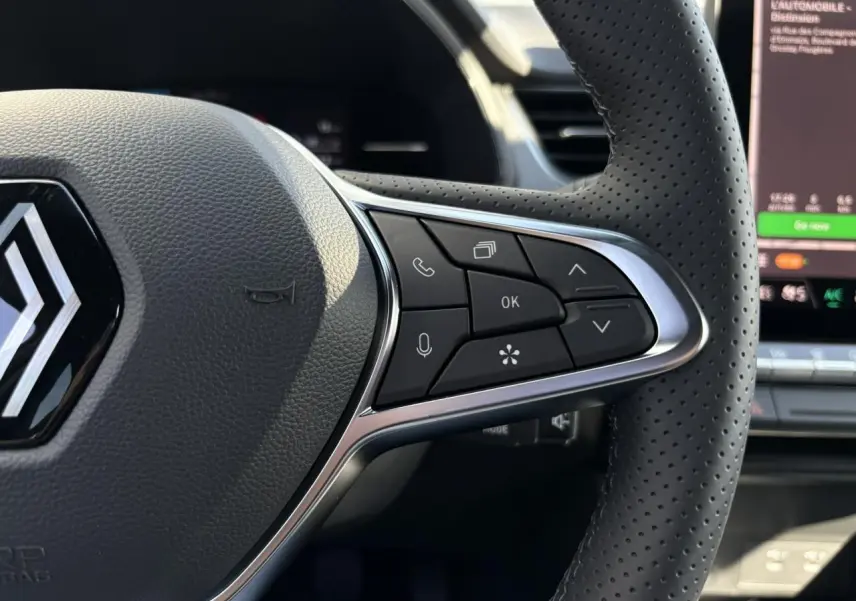 Gros plan sur le volant perforé du Renault Captur 2025 avec commandes multifonctions et logo au centre.